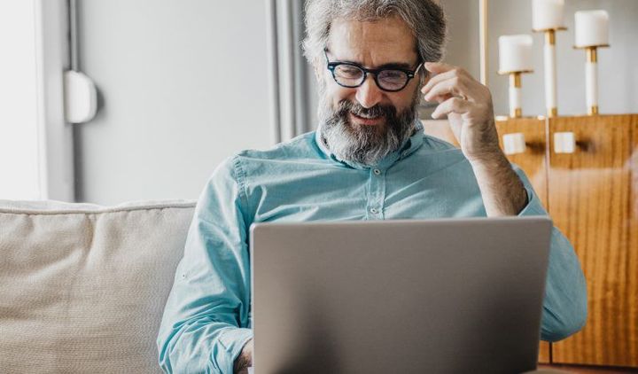 A man is sitting on a couch using a laptop computer.