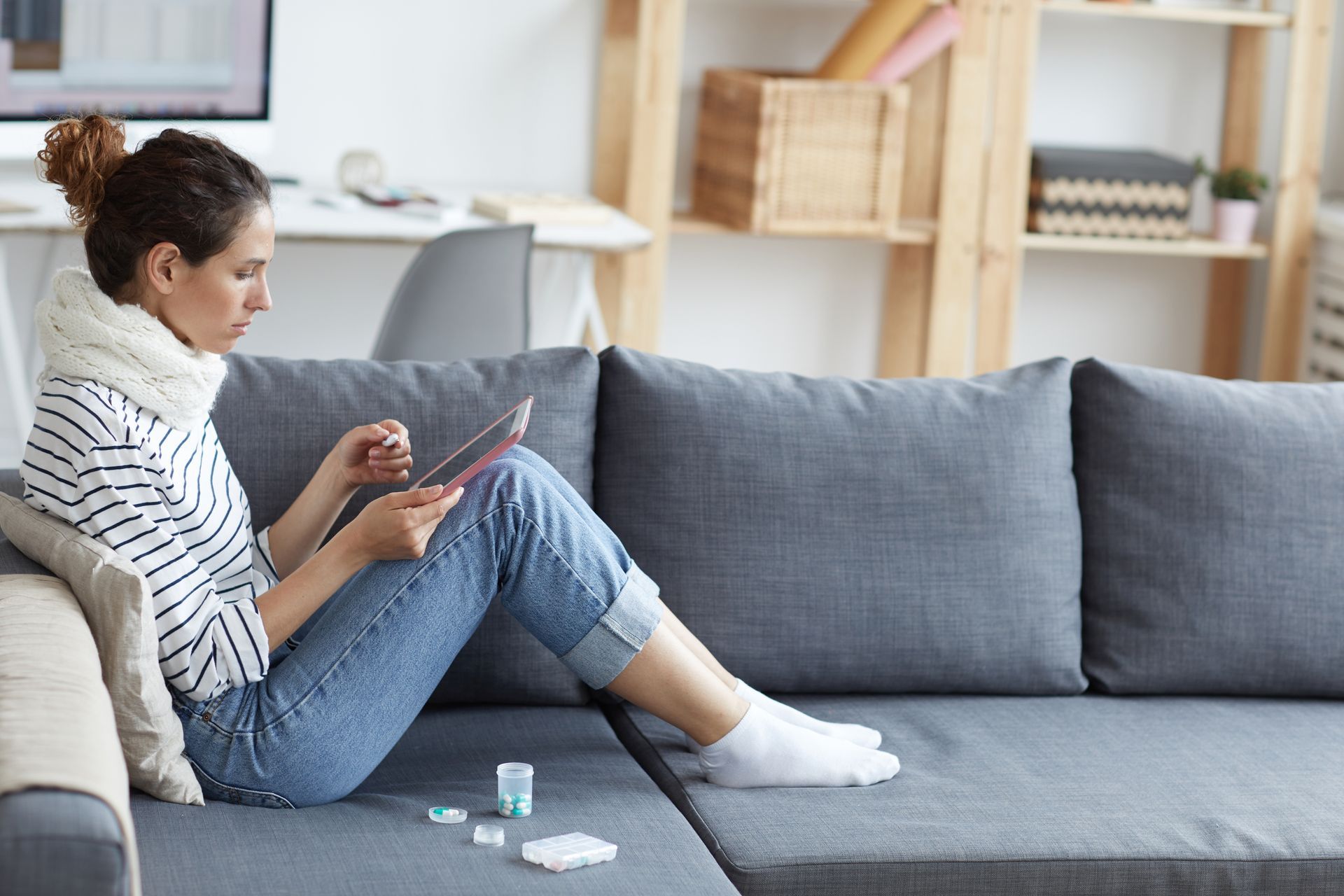 A woman is sitting on a couch looking at a tablet.