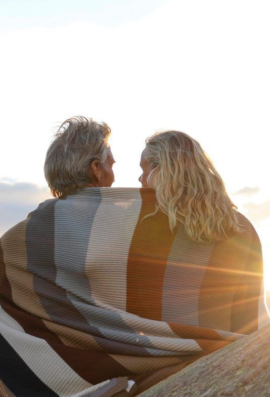 A man and a woman are wrapped in a blanket and looking at each other.