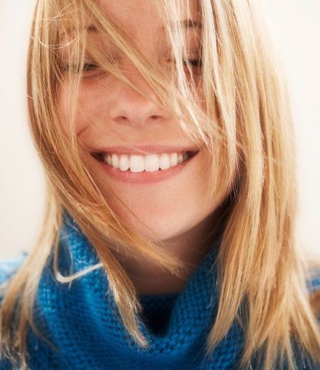 A woman wearing a blue scarf is smiling with her hair blowing in the wind