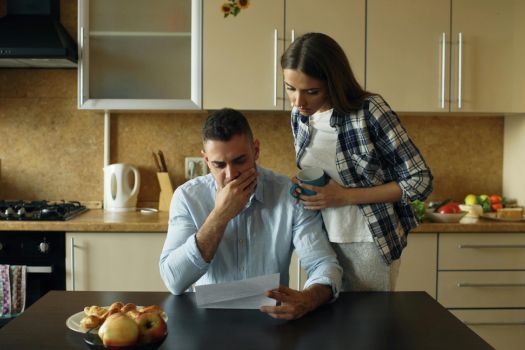 Person in a kitchen reading a document while another stands beside them, looking concerned.