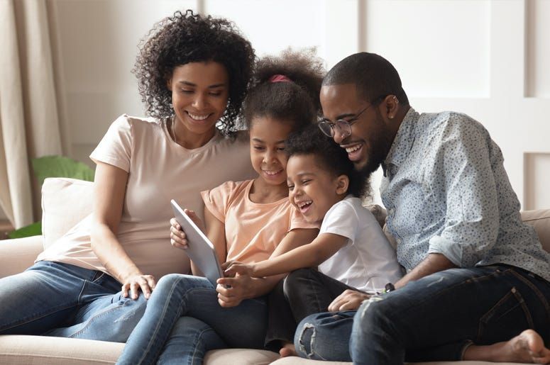 Family sitting on a couch, smiling and reading a book together in a bright living room