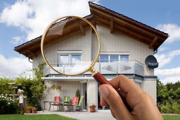 Hand holding magnifying glass over a suburban house, highlighting the upper windows and roof.