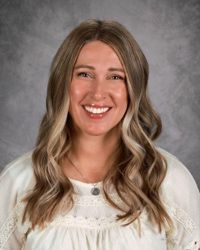 Portrait of a smiling woman with long wavy hair against a gray studio backdrop