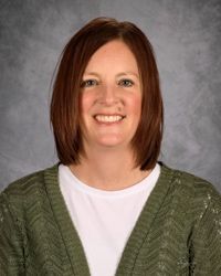 Portrait of a smiling person with shoulder-length brown hair, wearing a green sweater over a white shirt.