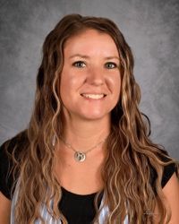 Portrait of a smiling woman with wavy brown hair against a gray studio backdrop