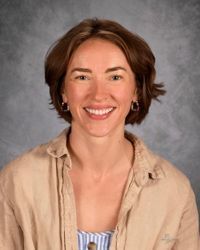 Smiling person in a beige shirt against a gray studio backdrop