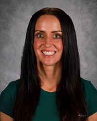 Portrait of a smiling person with long dark hair against a gray studio backdrop