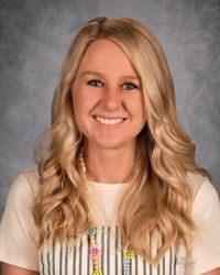 Smiling woman with long blonde hair in a white top against a gray studio backdrop