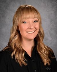 Smiling person with long blonde hair in a black shirt against a gray studio backdrop
