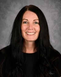 Smiling woman with long dark hair in a black top against a gray studio backdrop