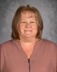 Portrait of a smiling person wearing a mauve blouse against a gray studio backdrop