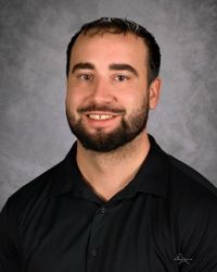 Studio portrait of a smiling man in a black collared shirt against a gray background