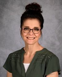 Portrait of a smiling woman with glasses and dark hair in a bun, wearing a green blouse on a gray background