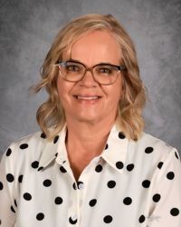 Smiling person in glasses and white polka-dot blouse against a gray backdrop