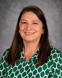 Smiling woman in a green patterned blouse against a gray studio backdrop