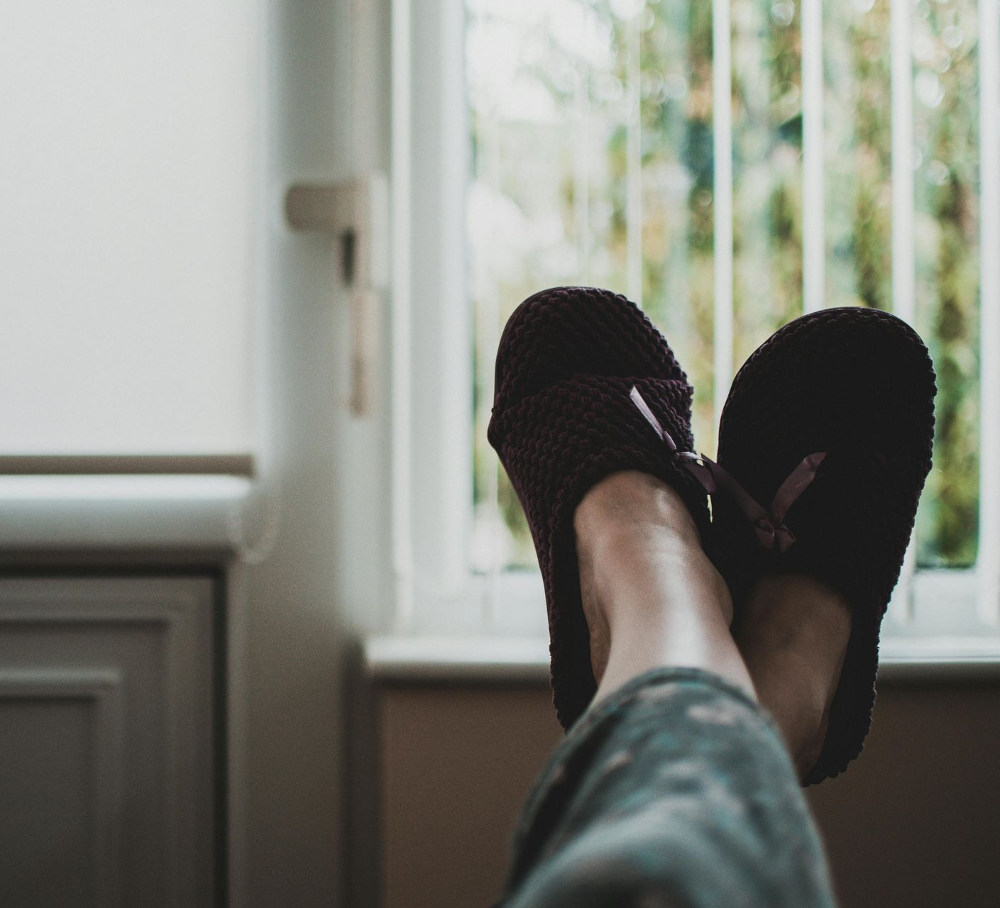 Een persoon met slippers aan en de voeten omhoog, voor een raam.
