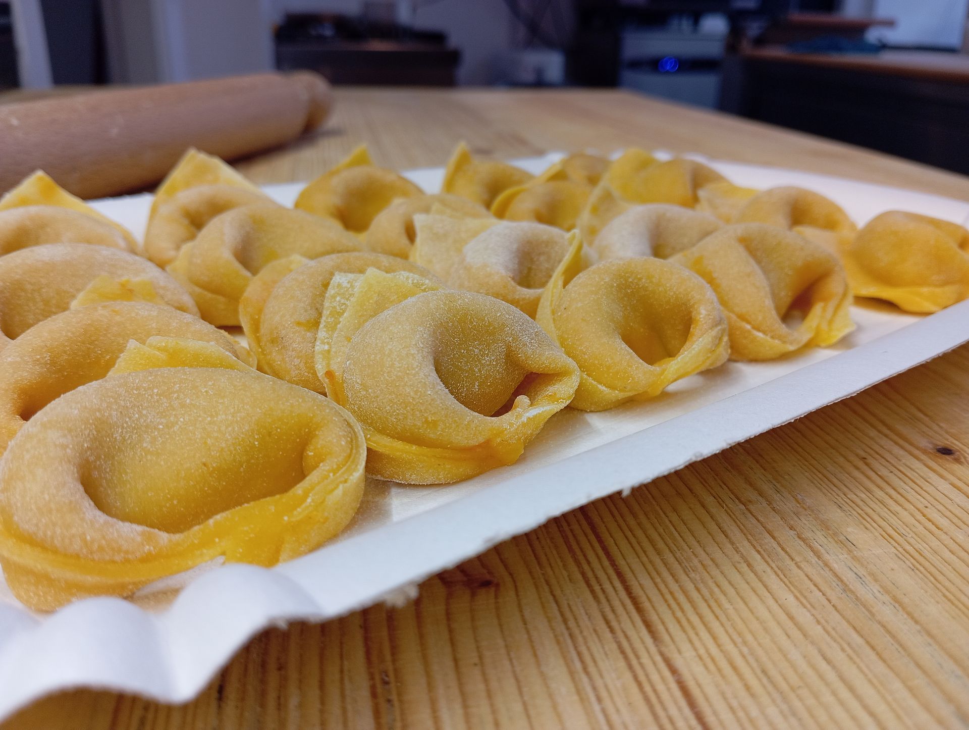Vassoio di tortellini crudi su un piano di lavoro in legno.