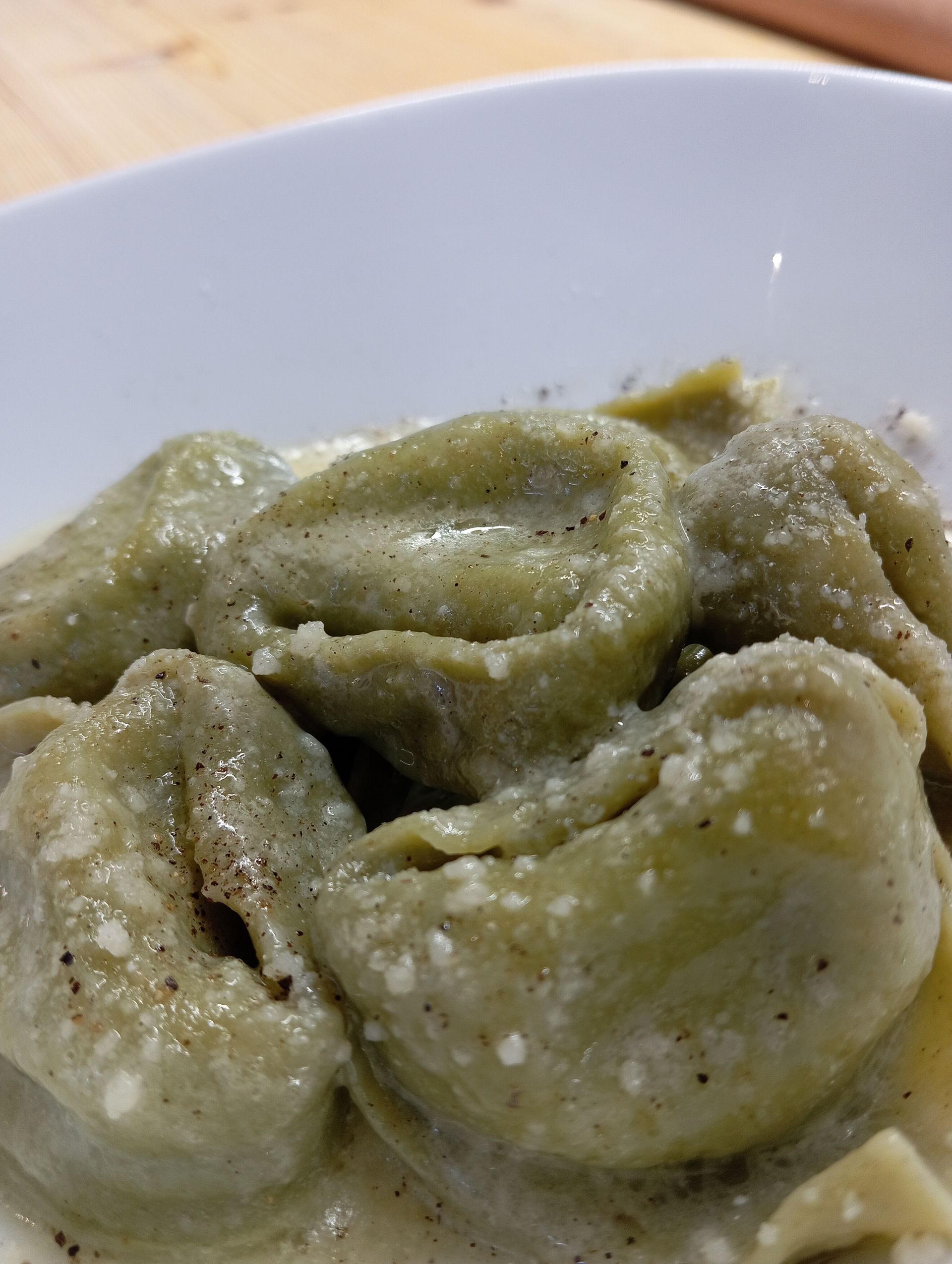 Primo piano di ravioli verdi in una ciotola bianca, guarniti con formaggio grattugiato.