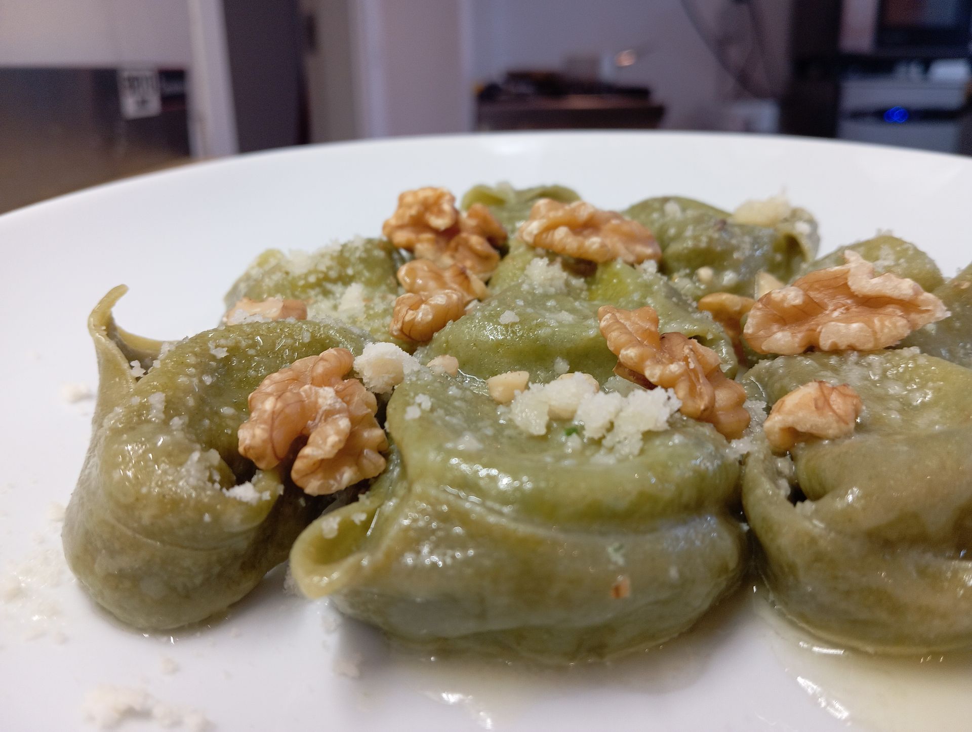 Pasta verde condita con pezzi di noci su un piatto bianco