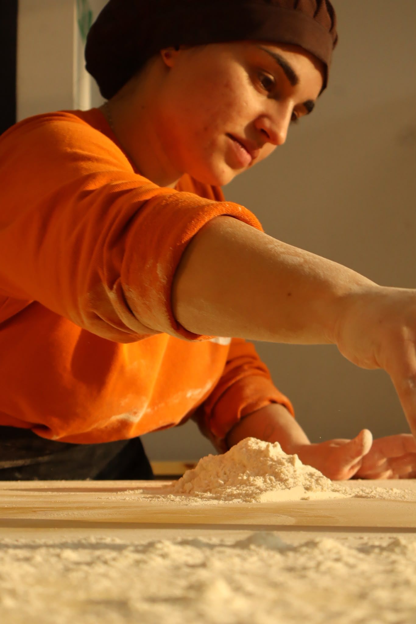 Una persona con una maglietta arancione modella l'impasto su una superficie infarinata in cucina.
