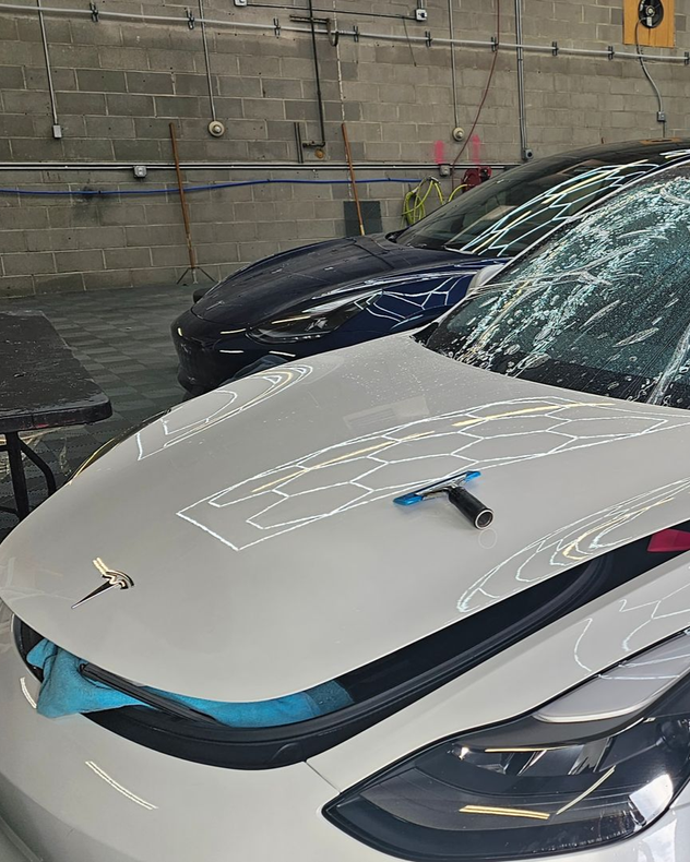 White car hood with tools on it, in a workshop beside a dark car and wet floor