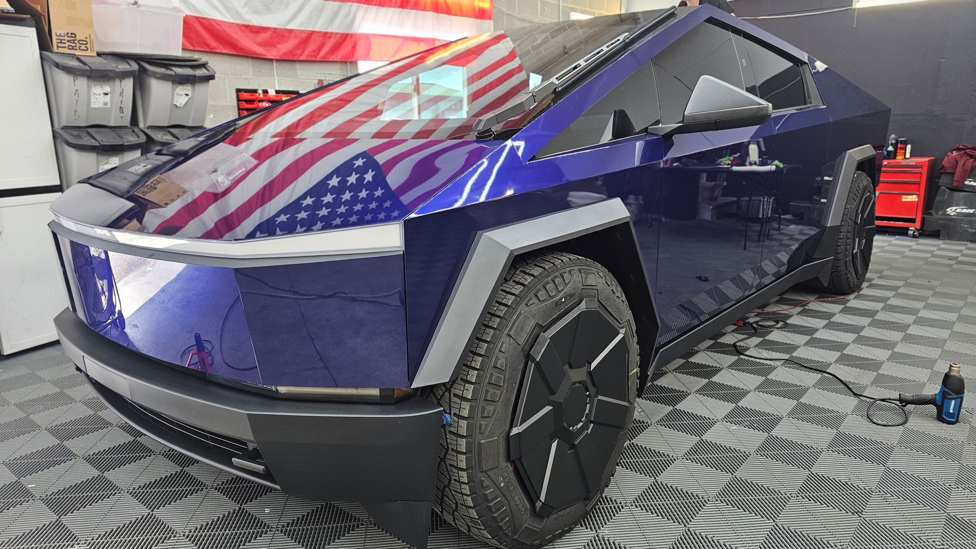 Red and blue wrapped Tesla Cybertruck in a garage, front-left view