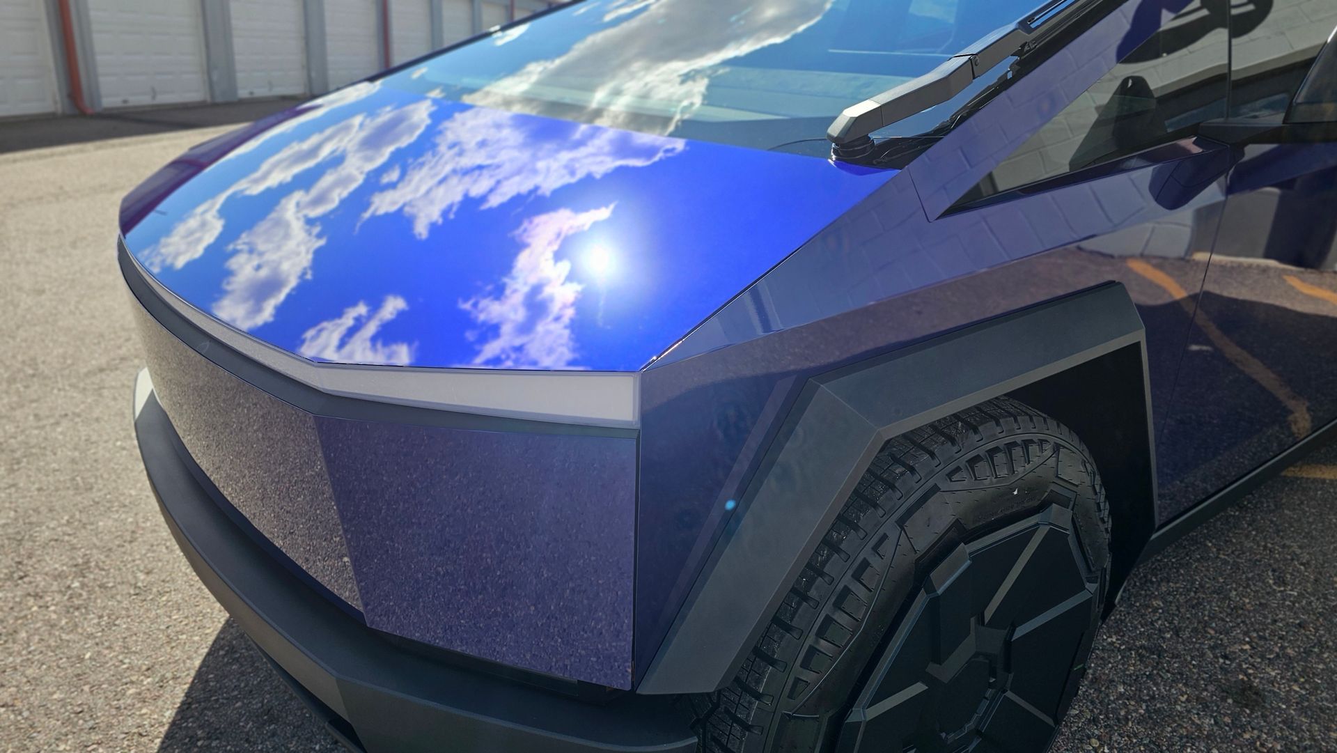 Front corner of a blue futuristic pickup truck with angular body panels and black off-road tires.