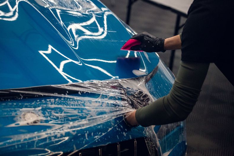 Person polishing a blue car hood with a cloth, creating a glossy reflection