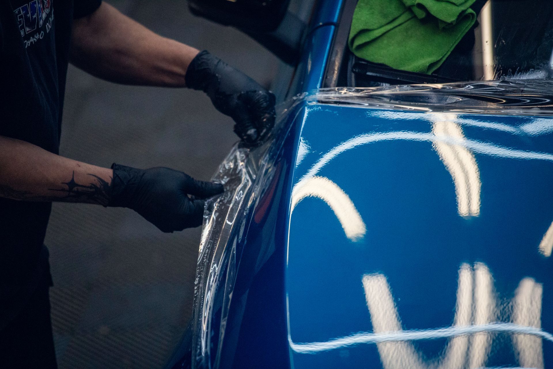 Gloved hands polishing a blue car’s body panel with reflections on the paint
