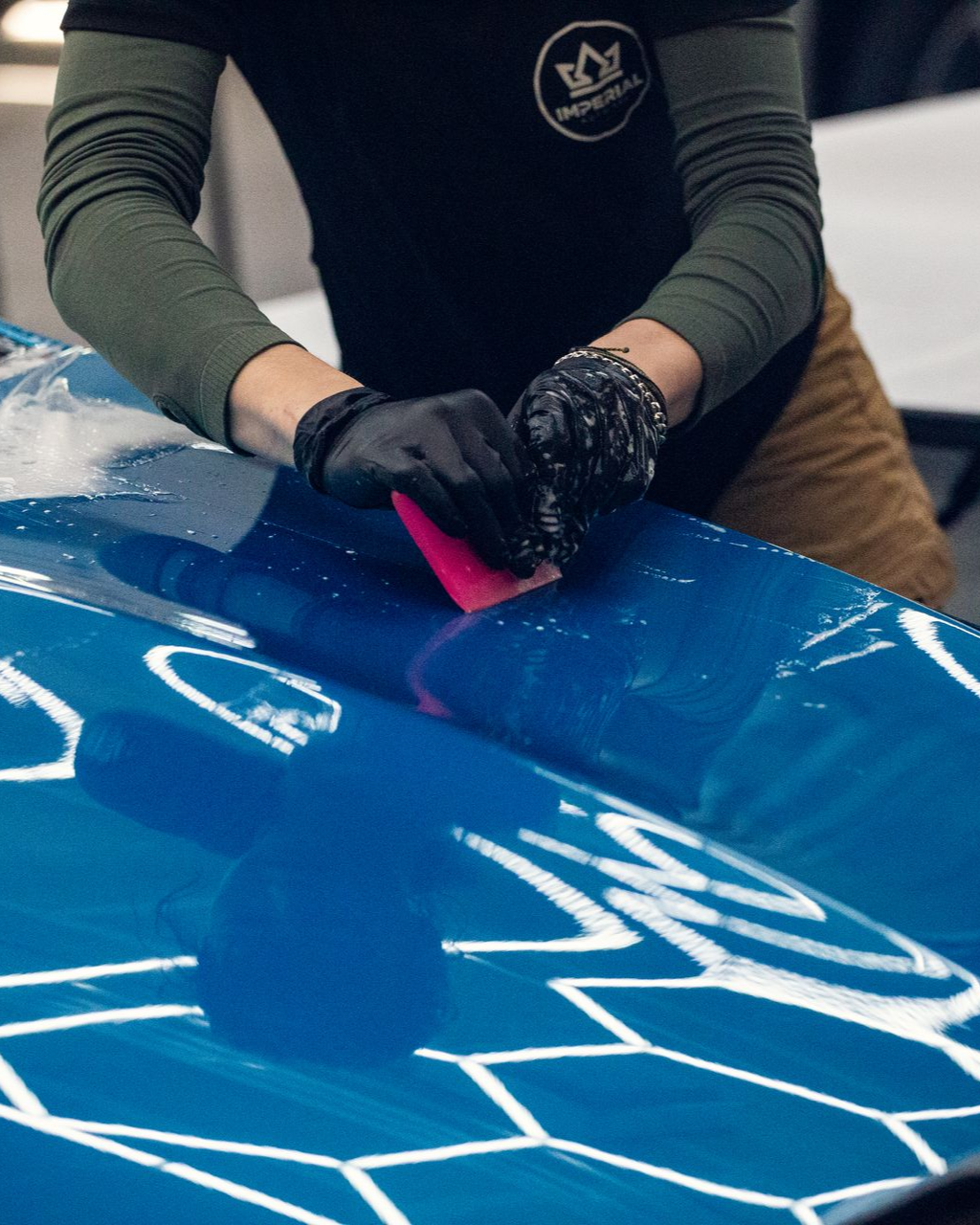 Person smoothing pink material on a blue car hood in a workshop
