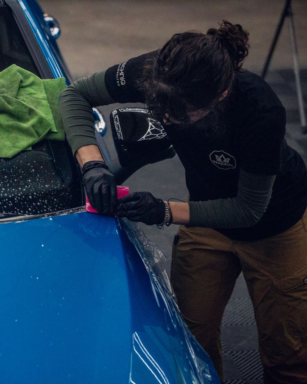 Person repairing a blue car hood with a tool in a dim garage