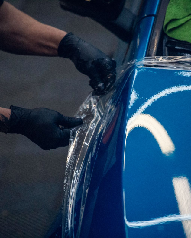 Gloved hands apply clear film to a blue car door panel.