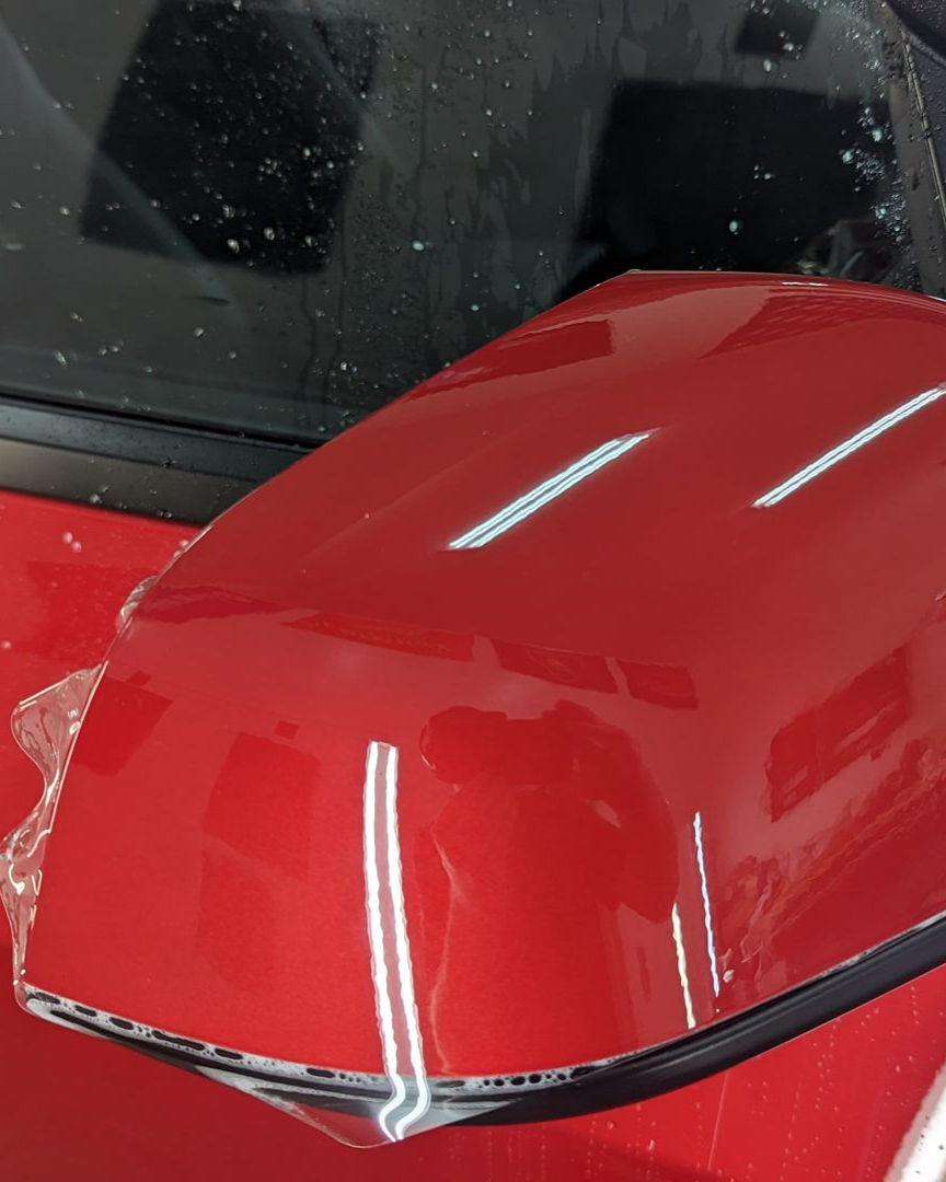 Red car hood with chrome trim parked by a wet windshield