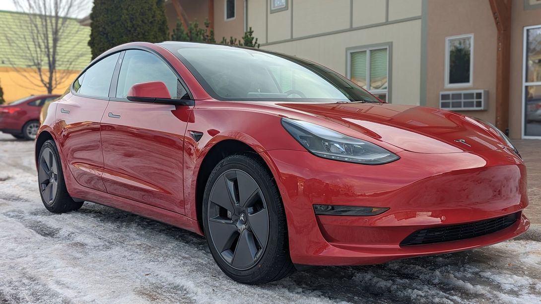 Red Tesla sedan parked on snowy pavement beside a building