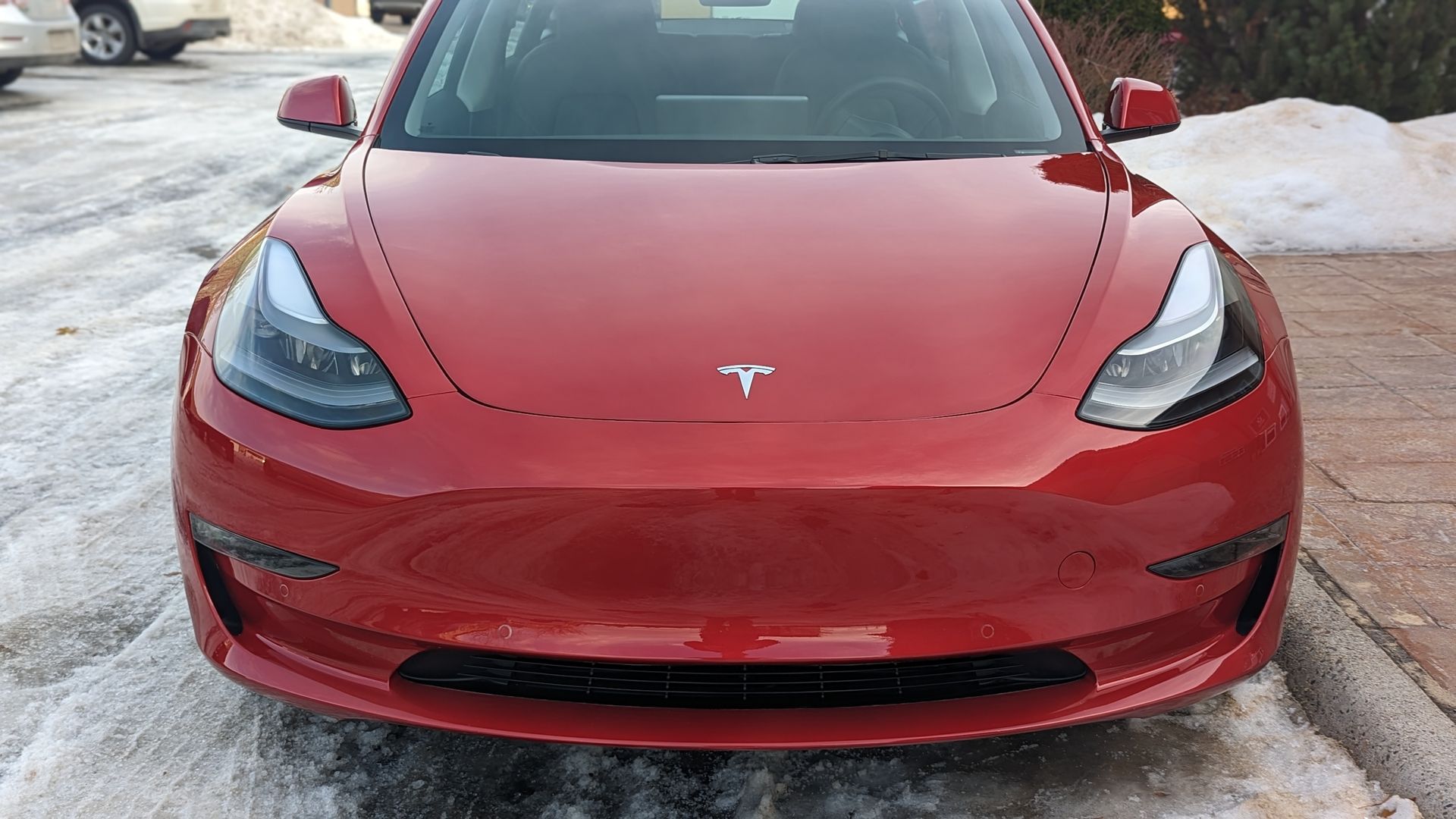 Front view of a red Tesla parked on a snowy lot.