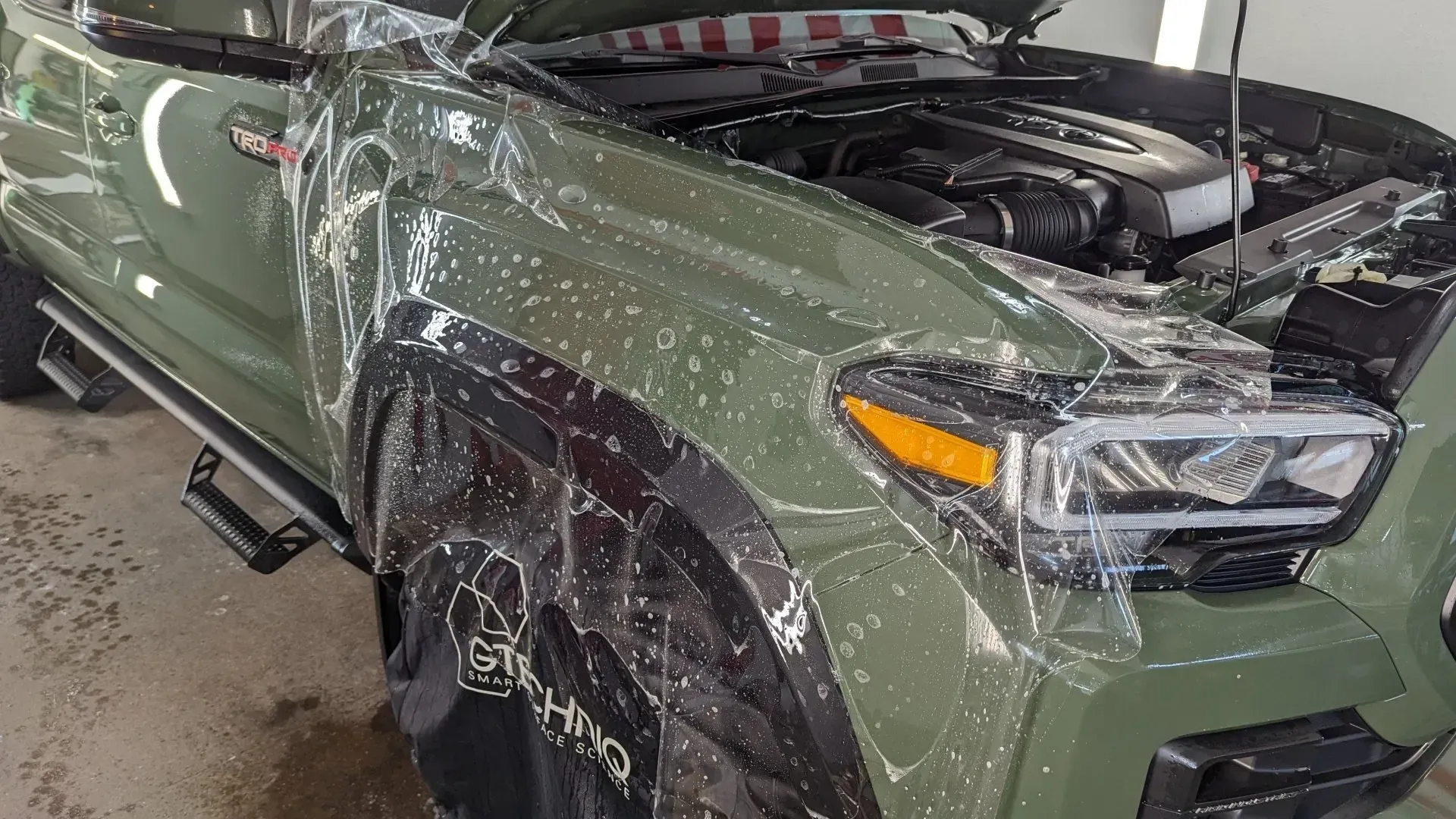 Green pickup truck front end covered in clear protective film in a garage