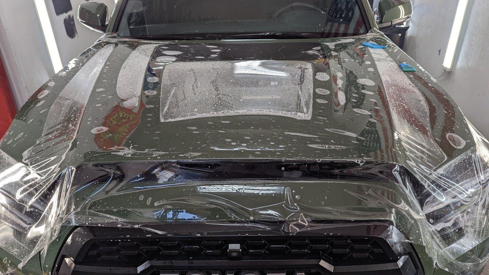 Car covered in protective plastic inside a workshop, front view with hood and windshield wrapped