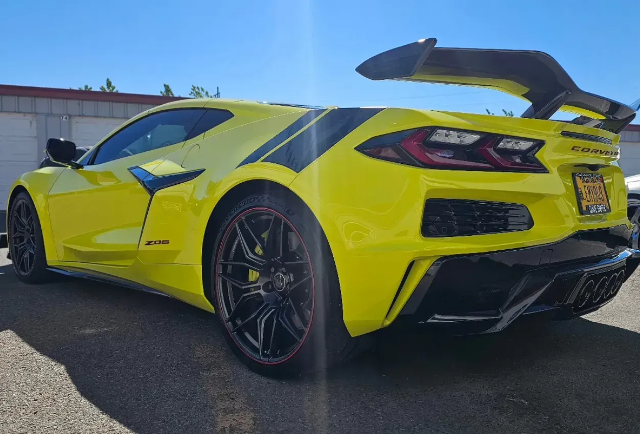 Yellow sports car with black accents parked outdoors, rear three-quarter view, under a blue sky