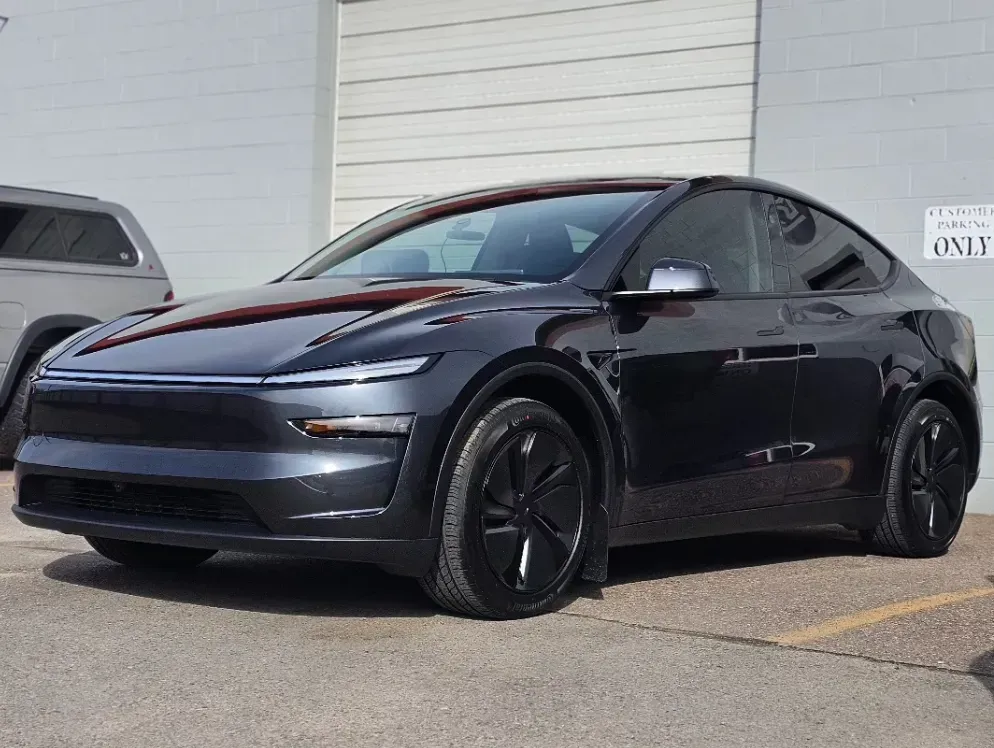 Dark gray Tesla sedan parked beside a white building