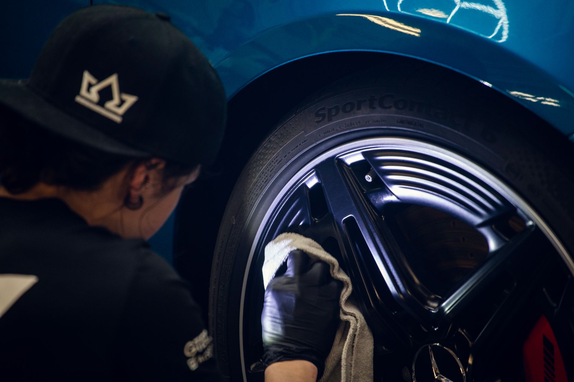 Mechanic inspecting a blue sports car’s wheel with a gloved hand in a garage