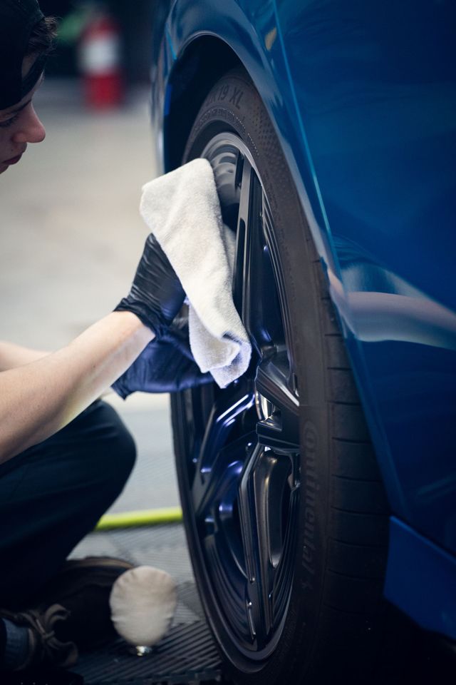 Person wiping a blue car wheel with a white cloth in a garage
