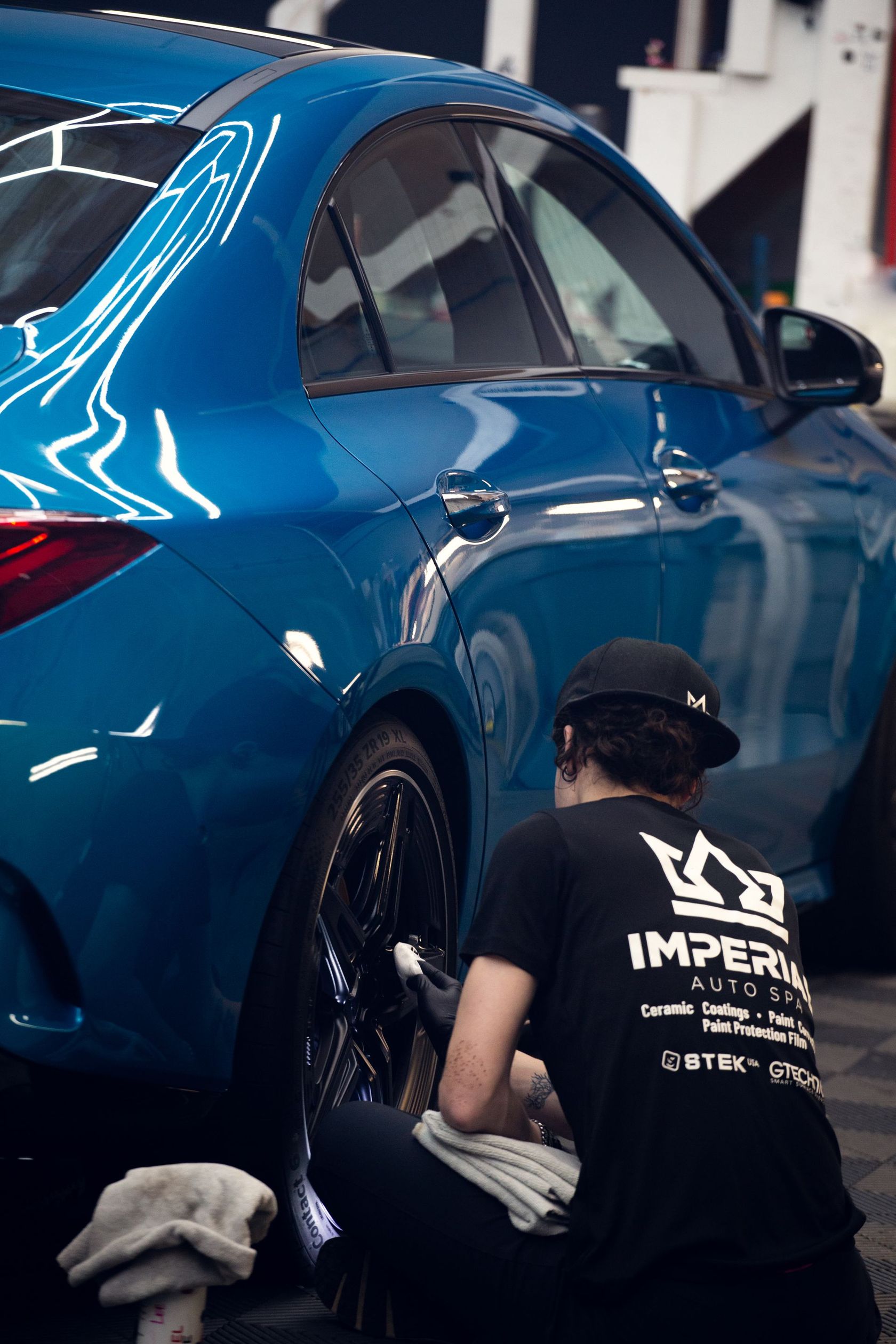 Worker polishing a blue sports car’s rear quarter panel in a workshop
