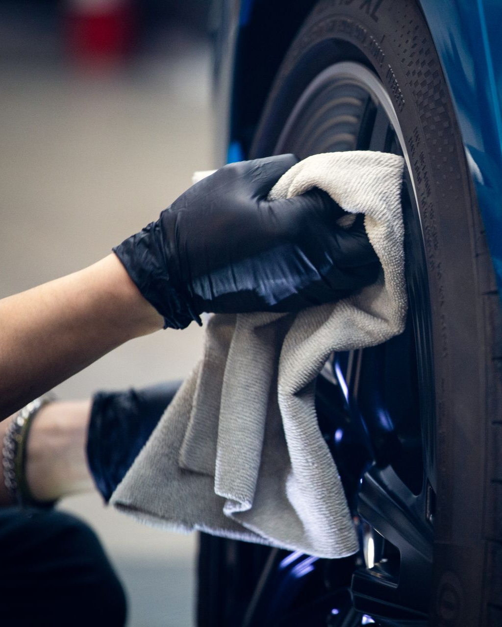 Gloved hand wiping a car wheel with a gray cloth