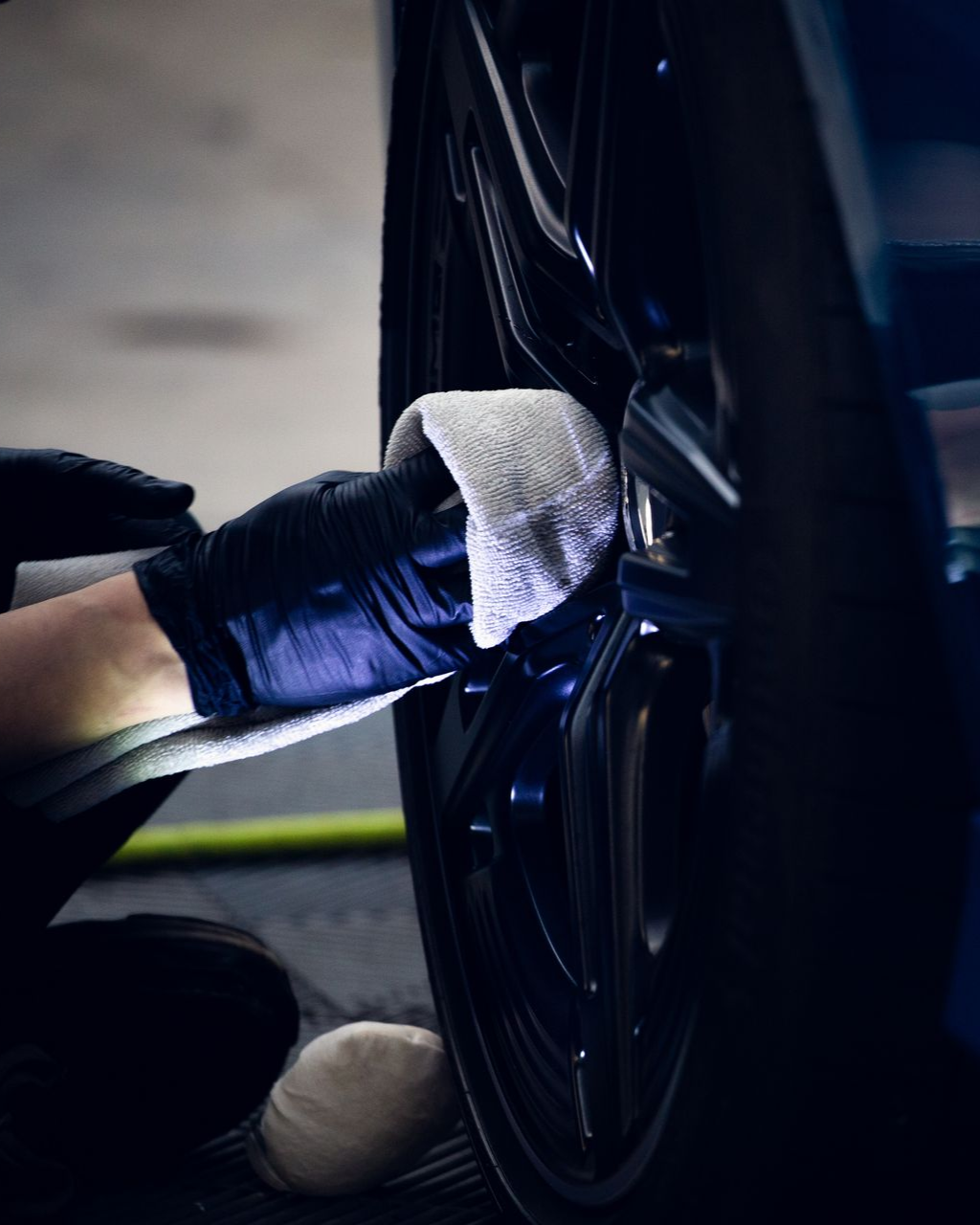 Gloved hand polishing a black car wheel with a white cloth