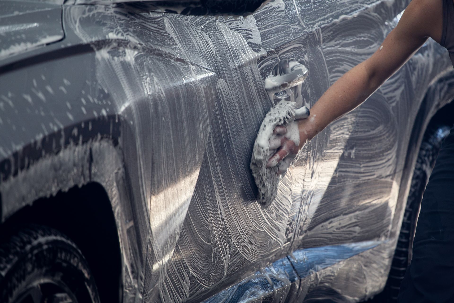 Person washing a black car with soap suds