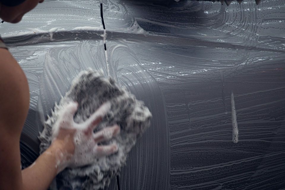 Hand washing a car with soap suds on a dark vehicle panel