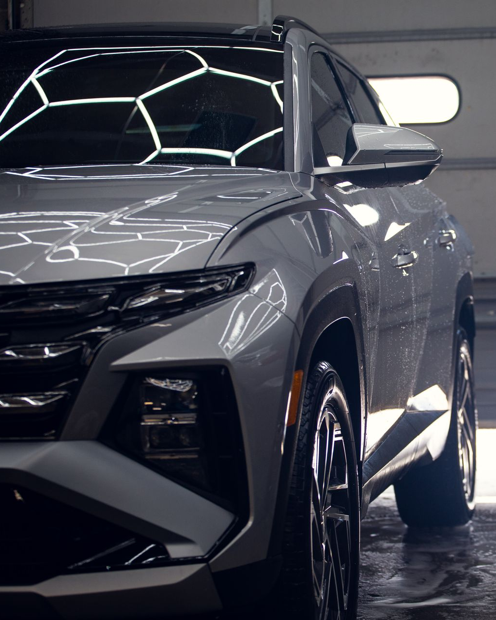 Gray SUV in a garage, front three-quarter view under bright ceiling lights