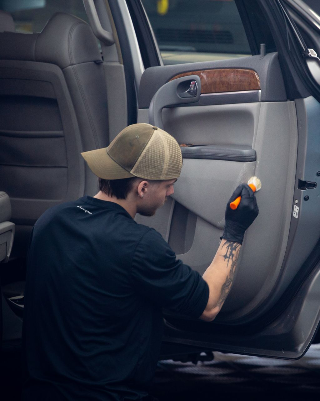 Person cleaning a car door interior with a brush, wearing gloves and a cap.