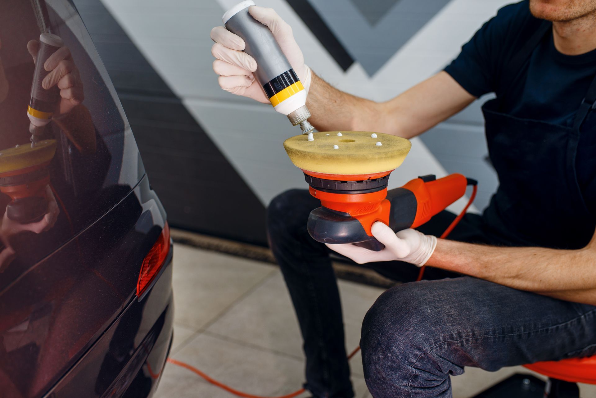 Person using a dual-action polisher to buff a red car in a garage